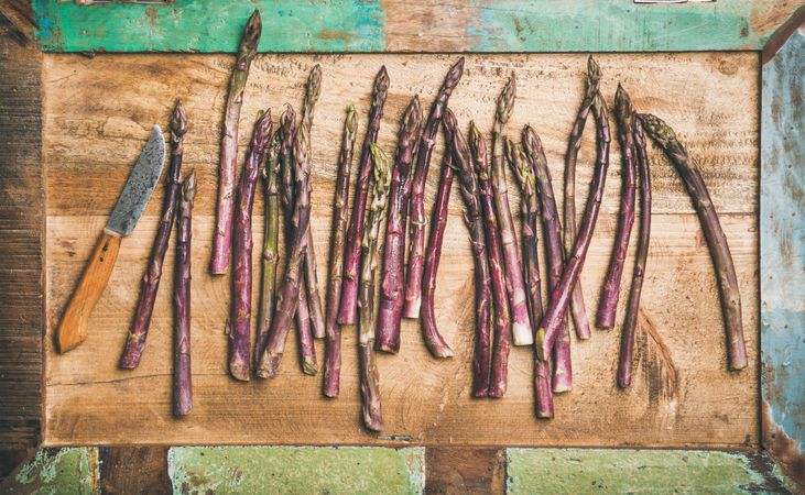 Scattered pieces of washed purple asparagus, on green trimmed wooden board