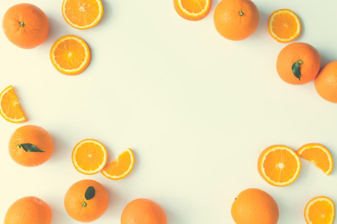 Oranges, whole and slices, and green leaves on cream background