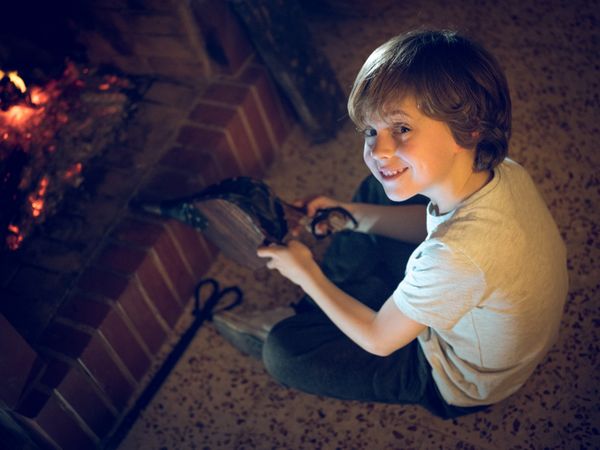 Preschool boy sitting at fireplace with bellows