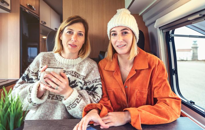 Two female friends looking at camera as if talking on video call from back of camper van