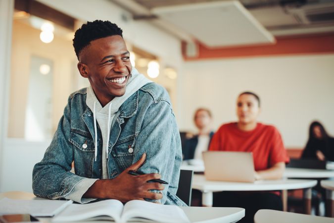 College student smiling while sitting in class with students behind him