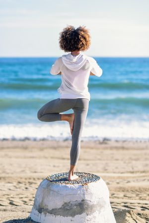 Back of Black woman doing exercise on one leg the beach