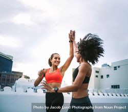 Two cheerful women in fitness wear giving high five while running on the terrace 5RkDR4