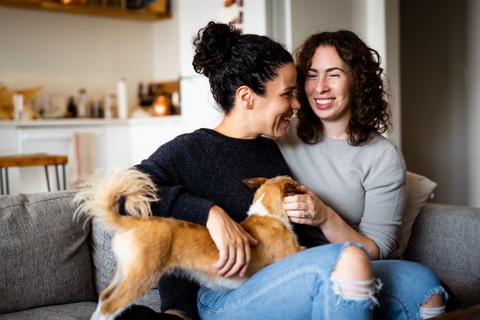 Female couple smiling and relaxing at home on sofa with pet dog