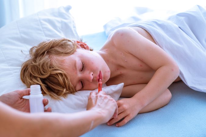 Crop mother giving medicine to sleeping son