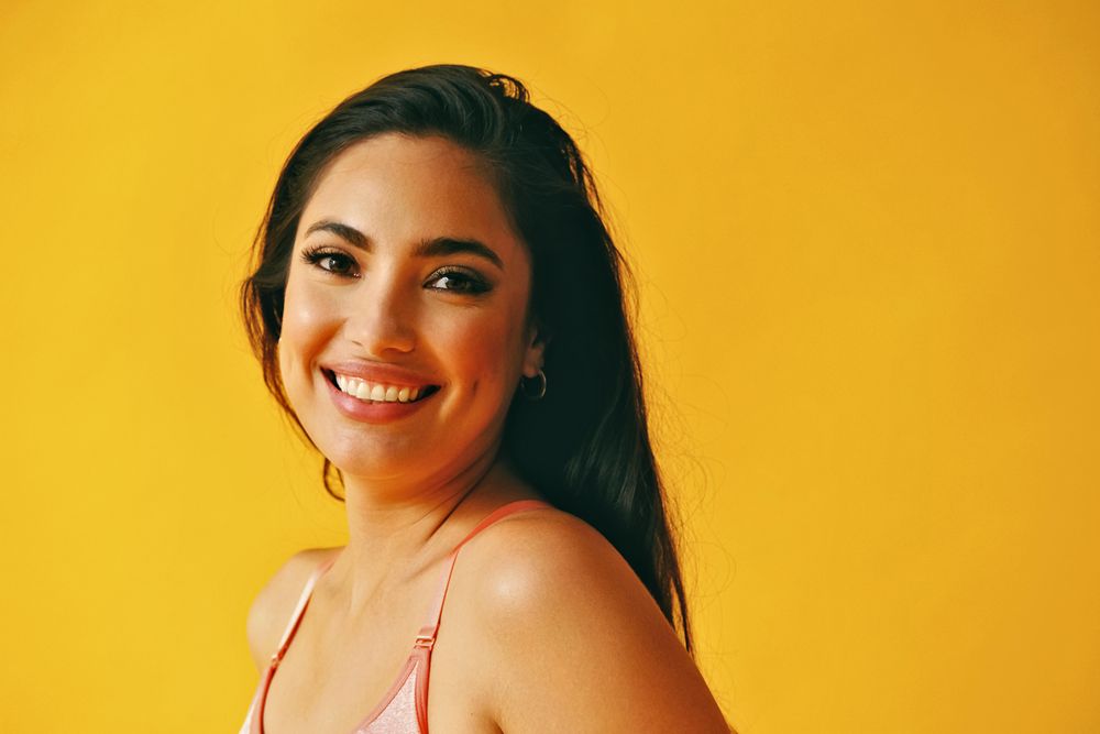 Headshot of smiling confident Hispanic woman standing in front of a yellow background