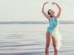 Ballerina in swimsuit with tutu performing classical position in water