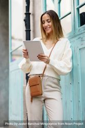 Happy woman in cream standing outside with digital tablet bGR2Nl