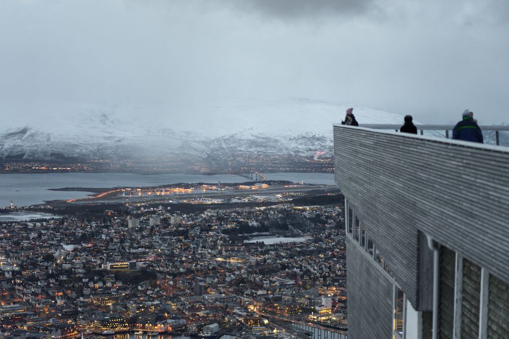 Tourists enjoying wonderful view of city against snowy mountain standing on viewpoint in evening