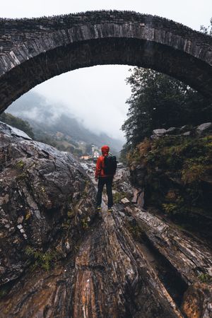 Back view of a man in red jacket with backpack walking under bridge in Switzerland