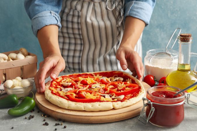Woman hold raw pizza on gray background with ingredients for cooking