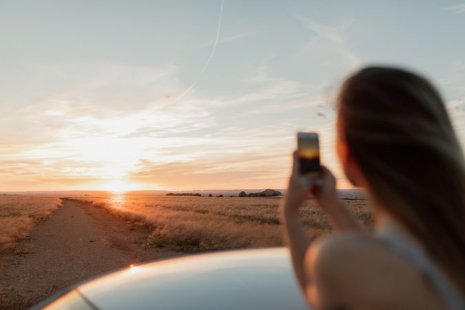 Young woman  taking a phone photo of a sunset with focus on the sun