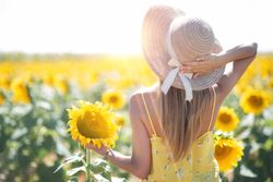 Woman in straw hat gazing while standing on bright sunflower field