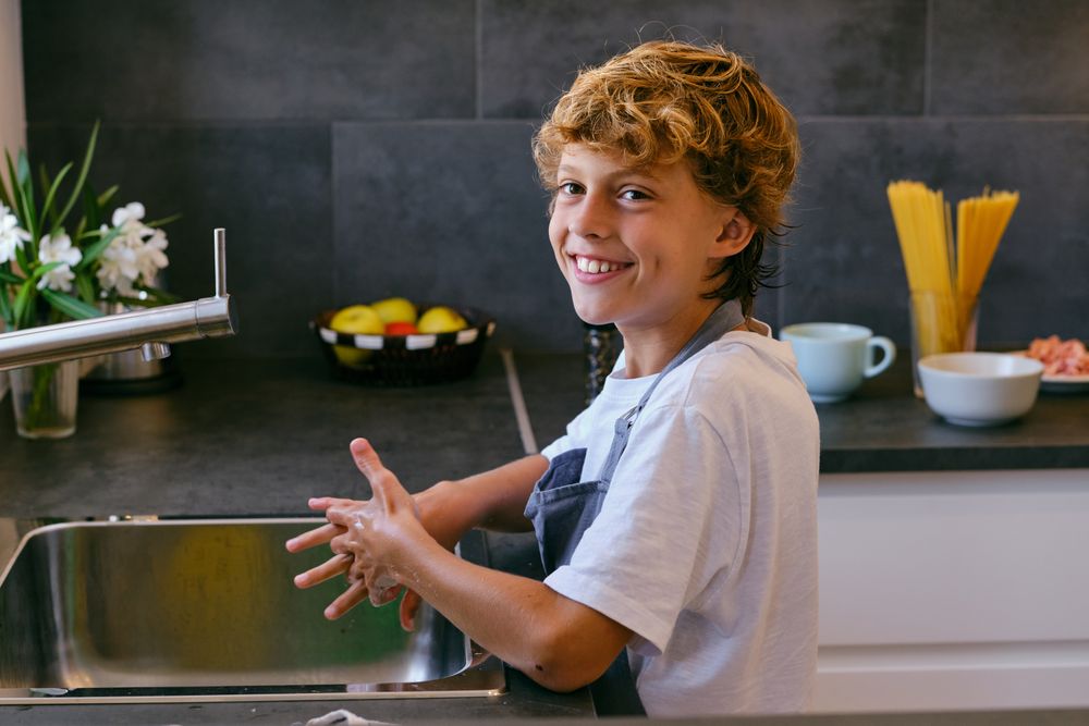 Smiling boy washing hands over sink in kitchen