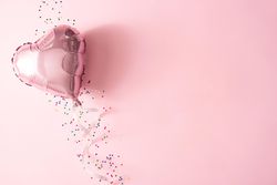 Pink foil balloon and confetti against pink background
