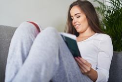 Smiling woman reading book and sitting on settee