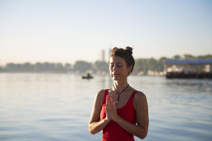 Woman relaxing with eyes closed and hands together near lake in the morning