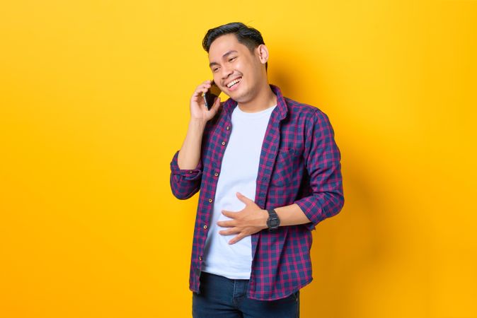 Laughing Asian male listening on cell phone in yellow studio shoot