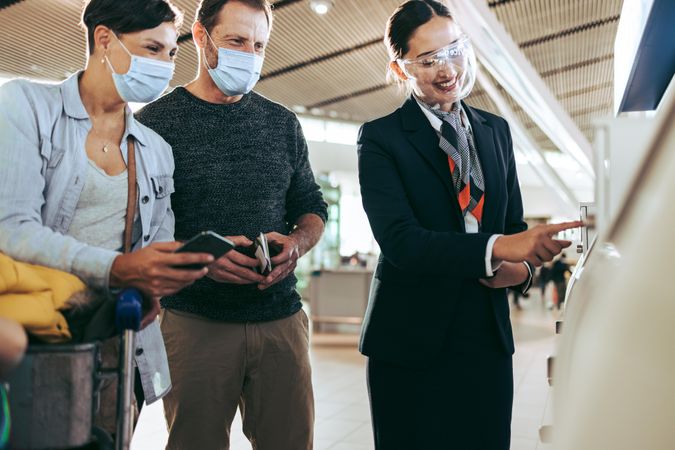Man and woman in face masks helped by airlines attendant at airport in pandemic