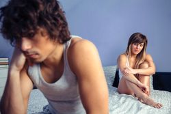 Woman sitting on bed looking over at angry man