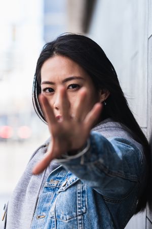 Asian brunette woman with long hair leaning on the wall and looking at camera