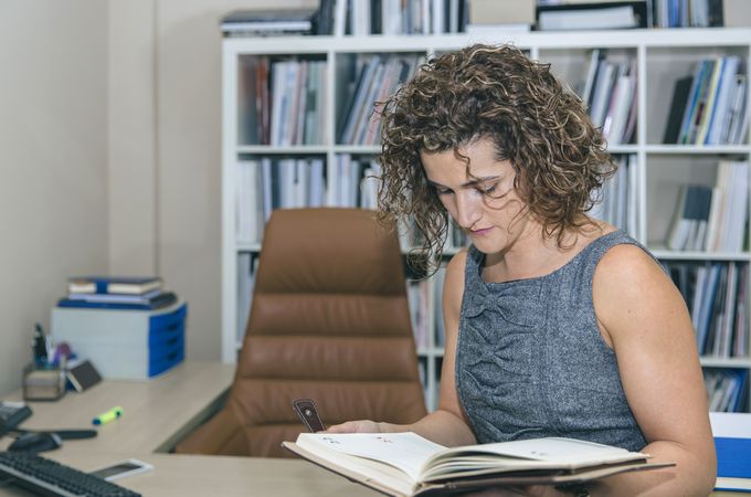 Businesswoman reviewing notebook in office with bookcase