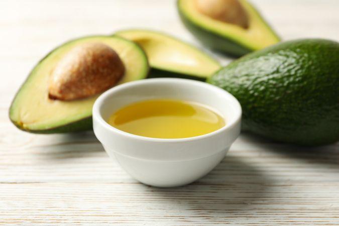 Ripe fresh avocado and oil on wooden background, close up