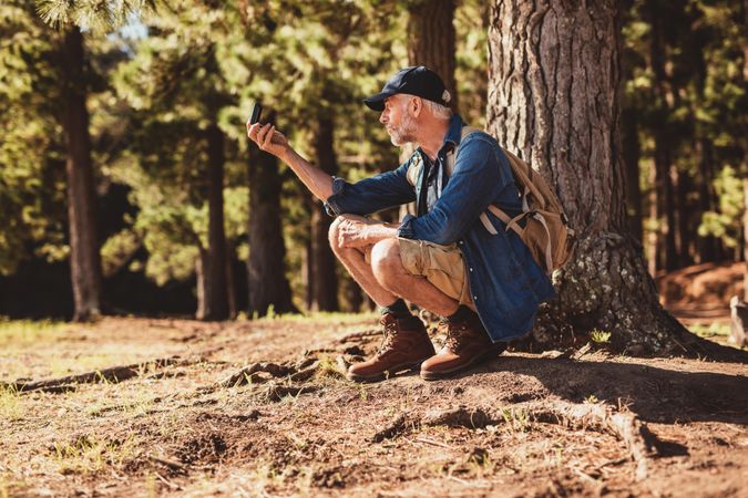 Mature man stops to check his position by using a compass while out on hike in the forest