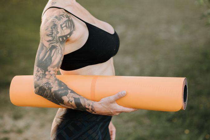 Woman with full sleeve holding orange yoga mattress