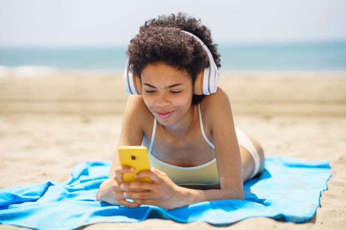 Female with curly hair on beach towel checking phone