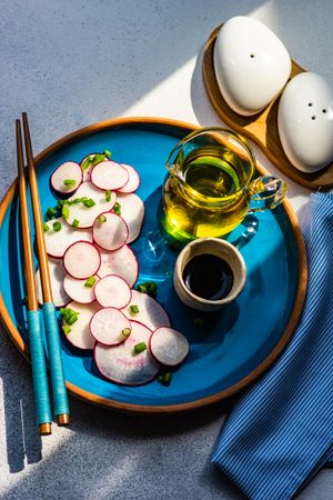 Top view of sliced radishes on blue plate served with oil and chopsticks