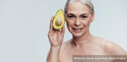 Mature woman holding up an avocado and looking at camera 4A3Gq0