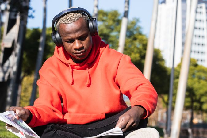 Serious Black man reading newspaper and listening to music in city park