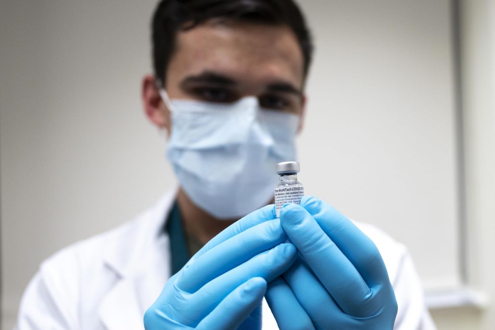 Gloved hands holding COVID vaccine vial