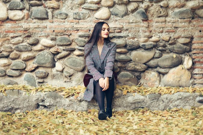 Female looking away in warm winter clothes sitting in front of rock wall in fall