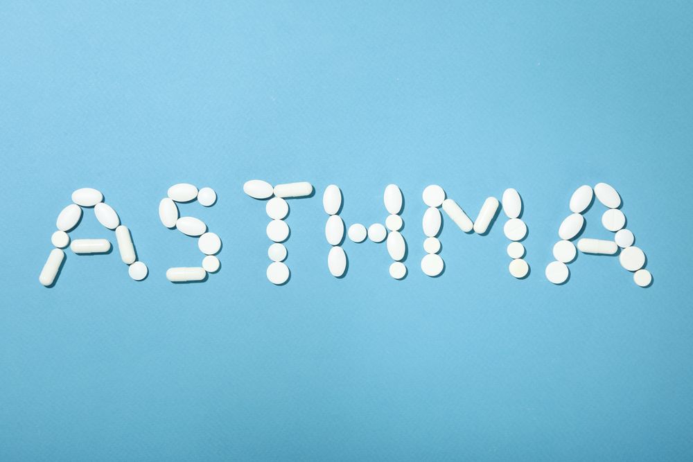 Pills on blue background spelling out “asthma”