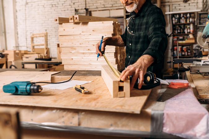 Mature male carpenter extending measuring tape on wooden block