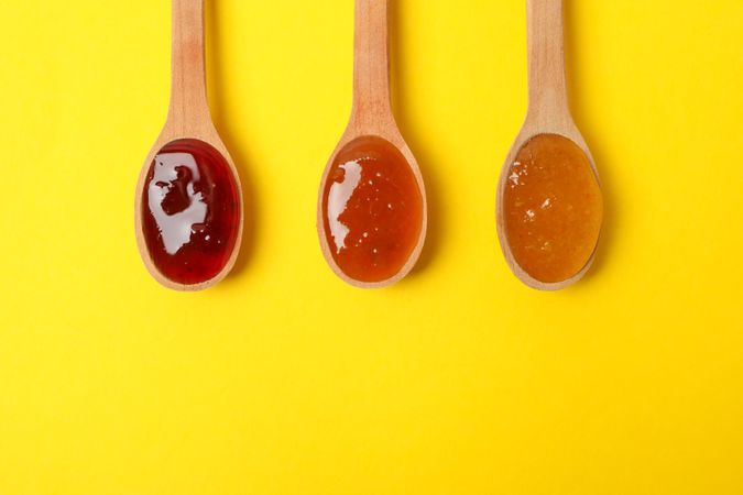 Spoons with jam on yellow background, top view