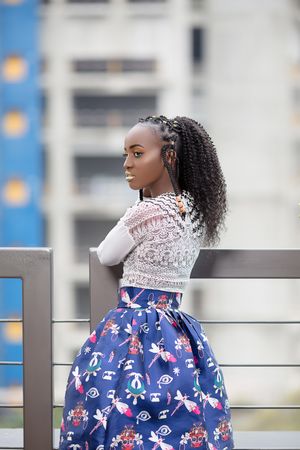 Side view of young woman in light top and blue floral skirt standing beside railing outdoor