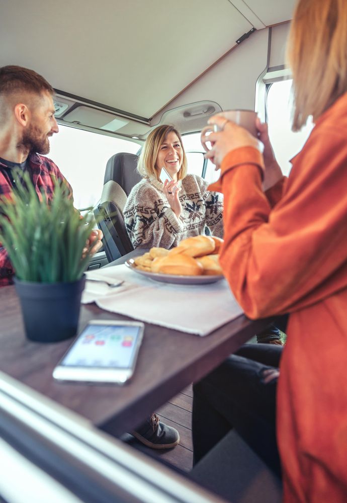 Friends enjoying coffee and pastries in back of camper, vertical