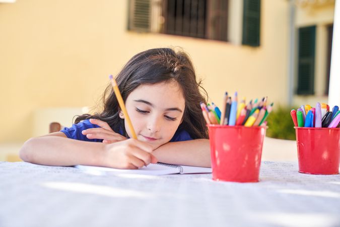 Cute girl drawing in copybook with pencils at table