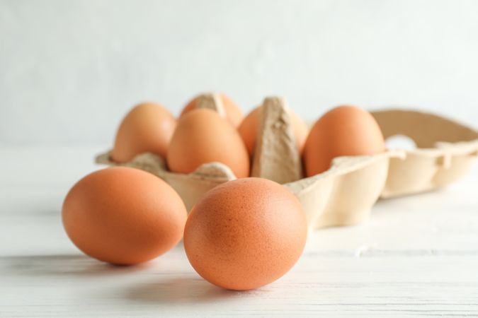 Chicken eggs in carton box on wooden table against light background