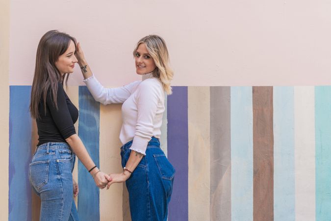 Happy girlfriends sitting against painted urban wall