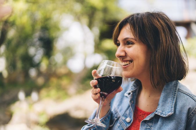 Woman happily taking a sip from a glass of red wine outside