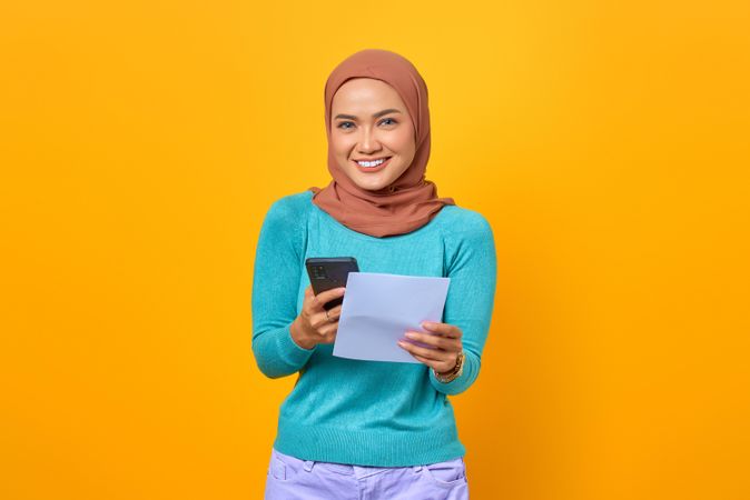 Smiling Muslim woman holding smart phone and piece of paper