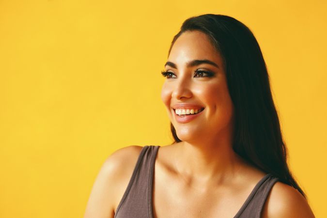Happy confident Hispanic woman looking away from camera in yellow room with her hand to her chin