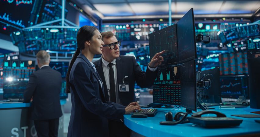 Asian Female and Male Stock Exchange Agents Using Desktop Computer, Discussing Investment Strategy for an International Business Client