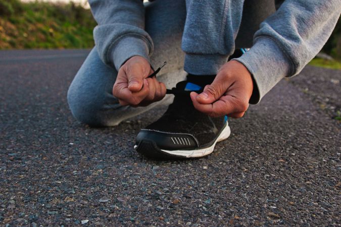 Person in gray sweater tying athletic shoes