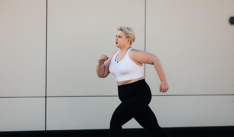 Young woman with short hair running outdoors at wall