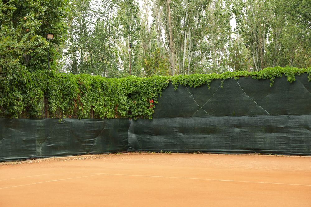 Clay tennis court with green fence, space for text